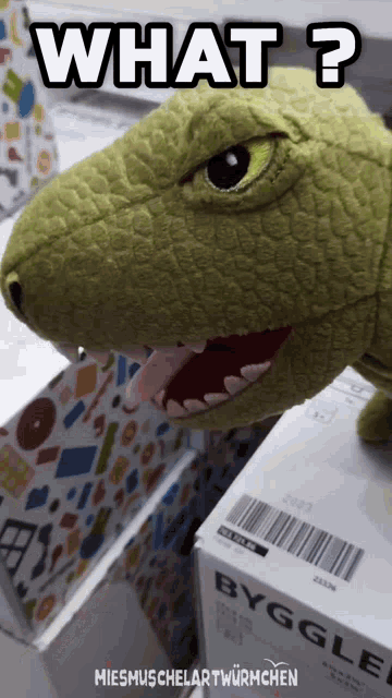 a stuffed dinosaur is sitting next to a box that says byggle