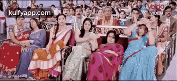 a group of women in saris are sitting in a stadium watching a game .