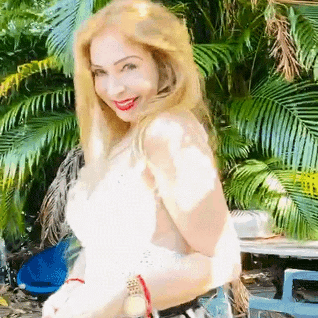 a woman in a white top is standing in front of a palm tree .