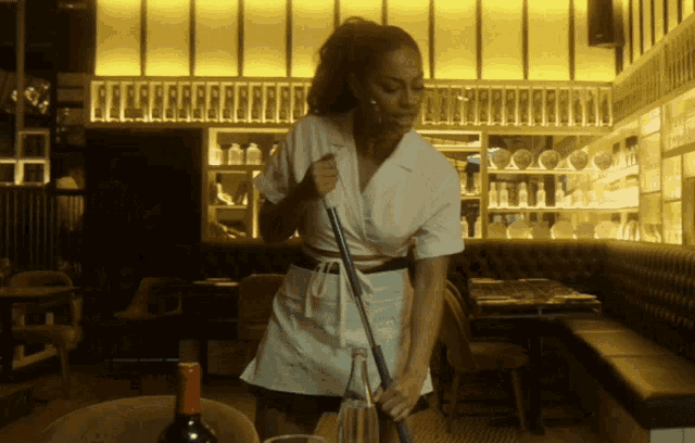 a woman in a white apron is sweeping a table in a restaurant