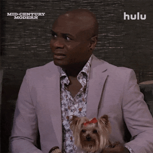 a man in a suit holds a small dog in front of a screen that says hulu