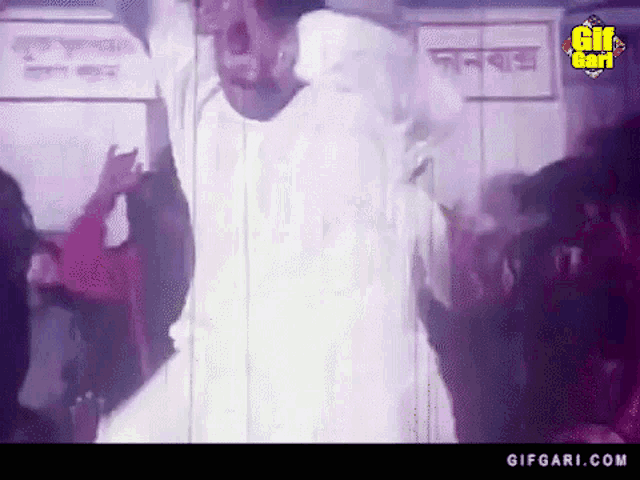 a man in a white shirt is dancing in front of a crowd in a room with a sign that says gifgari.com