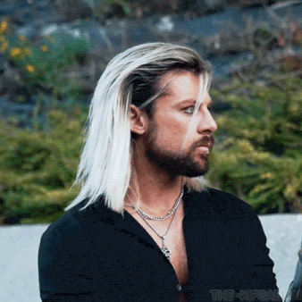 a man with long blonde hair and a beard is wearing a black shirt and a silver necklace .