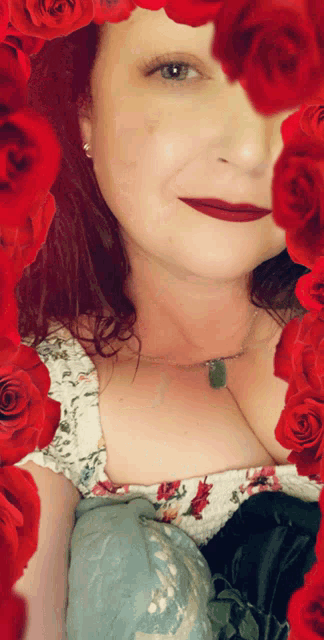 a woman is surrounded by red roses and has a green pendant around her neck