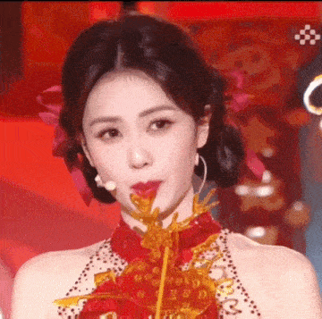 a woman in a red dress with a flower in her hair is holding a candy in her mouth .