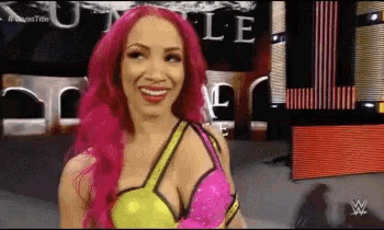 a woman with pink hair is smiling in front of a sign that says ' wwe ' on it