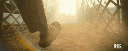 a close up of a person 's foot walking on a dirt road with a fence in the background .
