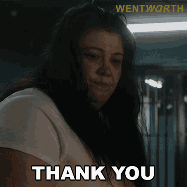 a woman in a white shirt says thank you in a dark room