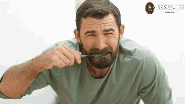 a man with a beard is brushing his teeth in front of a dr.squatch logo