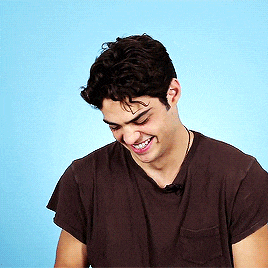 a young man wearing a brown shirt is smiling with his eyes closed