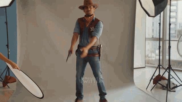 a man dressed as a cowboy holds two guns in front of a twitter banner