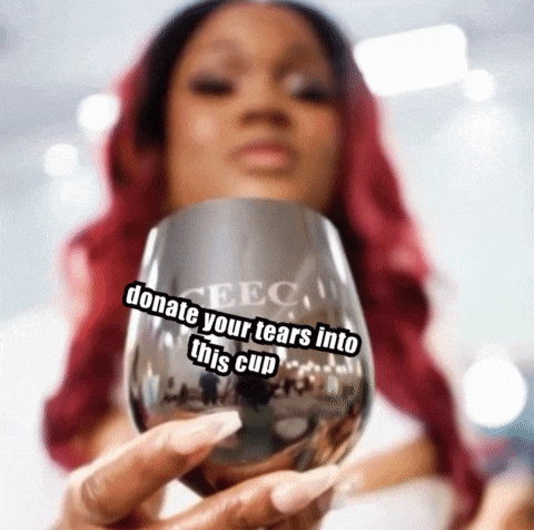 a woman with red hair is holding a wine glass with a sticker that says `` donate your tears into this cup '' .
