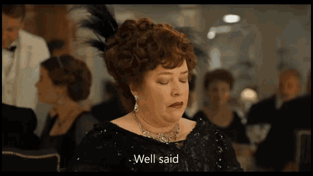 a woman in a black dress with a feather in her hair says well said