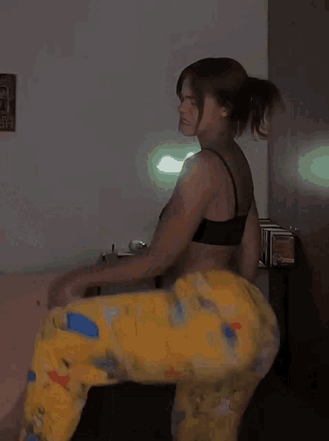 a woman in a black top and yellow pants is dancing in front of a table with books on it