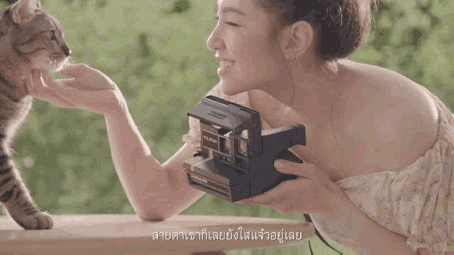 a woman holding a polaroid camera while a cat looks on