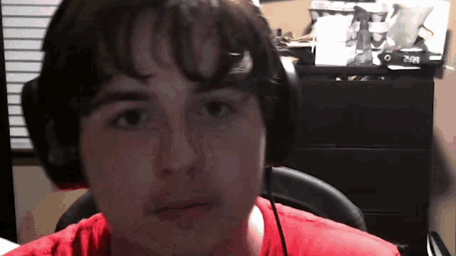 a man wearing headphones and a red shirt is sitting in front of a clock that reads 2:01
