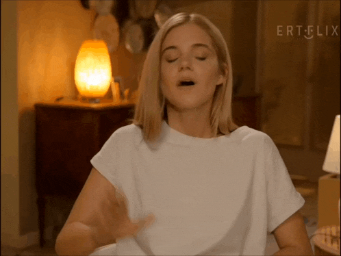 a woman in a white shirt is sitting in front of a lamp with her eyes closed and the words ertflix on the bottom