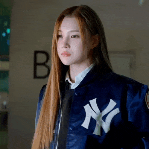 a woman wearing a blue ny yankees jacket looks at the camera