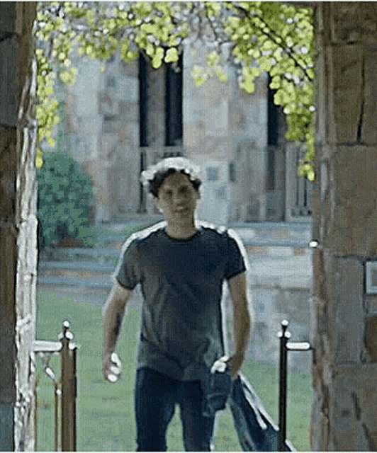 a man in a gray shirt is walking through a stone archway .