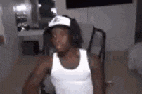 a man wearing a white tank top and a hat is sitting in a chair in a room .