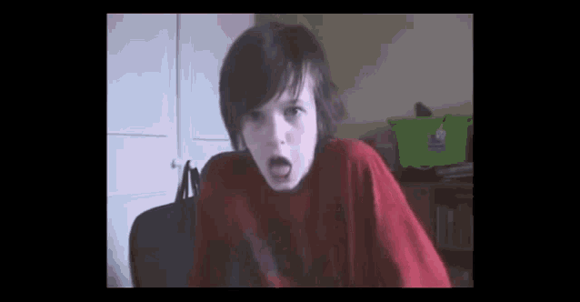 a young boy in a red shirt is making a face .