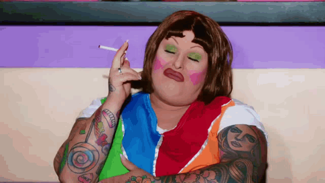 a woman with tattoos on her arms is smoking a cigarette while wearing a colorful shirt