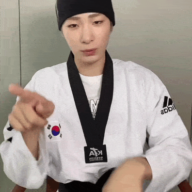 a man wearing a taekwondo uniform and a black belt is pointing at the camera .