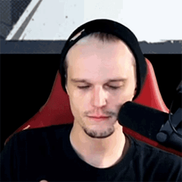 a man wearing a black beanie and a black shirt is sitting in front of a microphone .