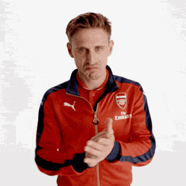 a man wearing a red fly emirates jacket holds his hands together
