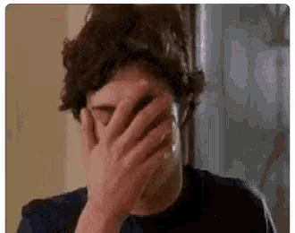 a man with curly hair is covering his face with his hands .
