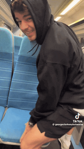 a man wearing a black hoodie is sitting on a train with blue seats