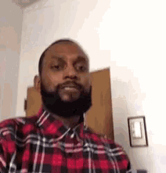 a man with a beard wearing a red and black plaid shirt is standing in a room .