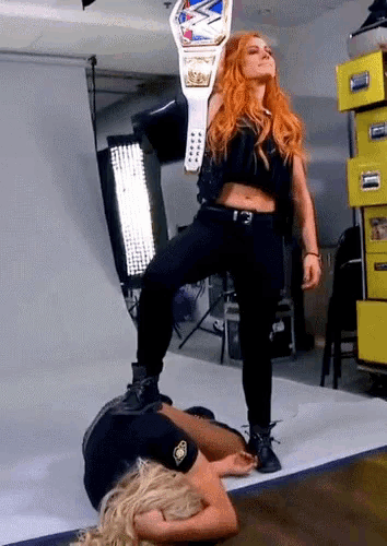 a woman is standing on another woman 's feet holding a wrestling belt