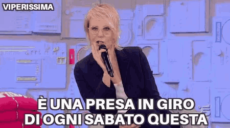 a woman is singing into a microphone with the words e una presa in giro di ogni sabato questa written below her