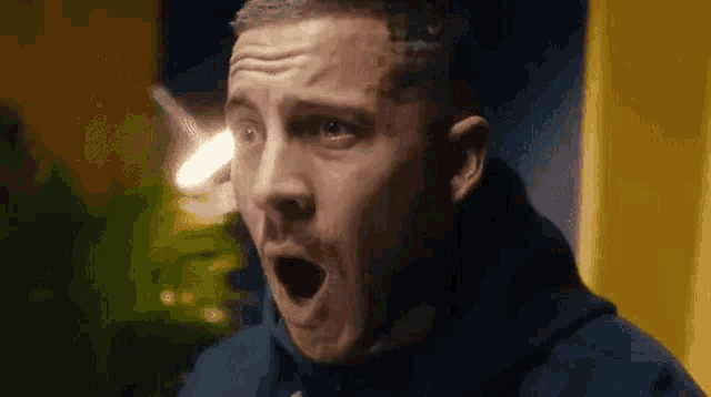 a man in a blue hoodie is making a funny face with his mouth open .
