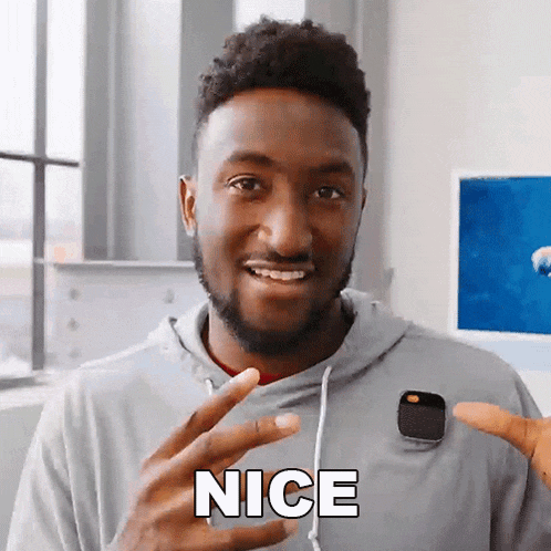 a man in a grey hoodie is holding a smart watch and saying nice .