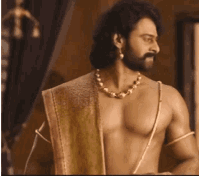 a shirtless man with a beard and a necklace is standing in a room and looking away .