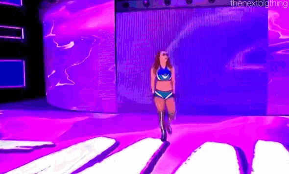 a female wrestler is walking down a purple and blue stage .