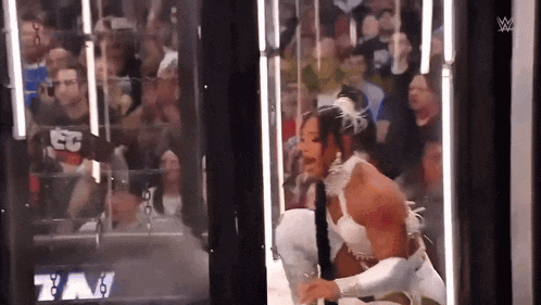 a man and a woman are wrestling in front of a crowd in a cage .