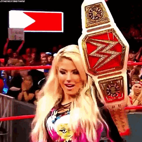 a woman in a wrestling ring is holding a championship belt over her head .