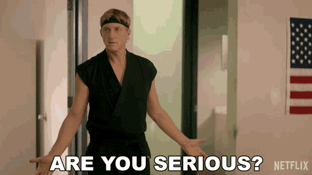 a man in a karate uniform says " are you serious " in front of an american flag