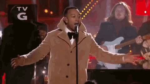 a man singing into a microphone with a tv g logo in the background