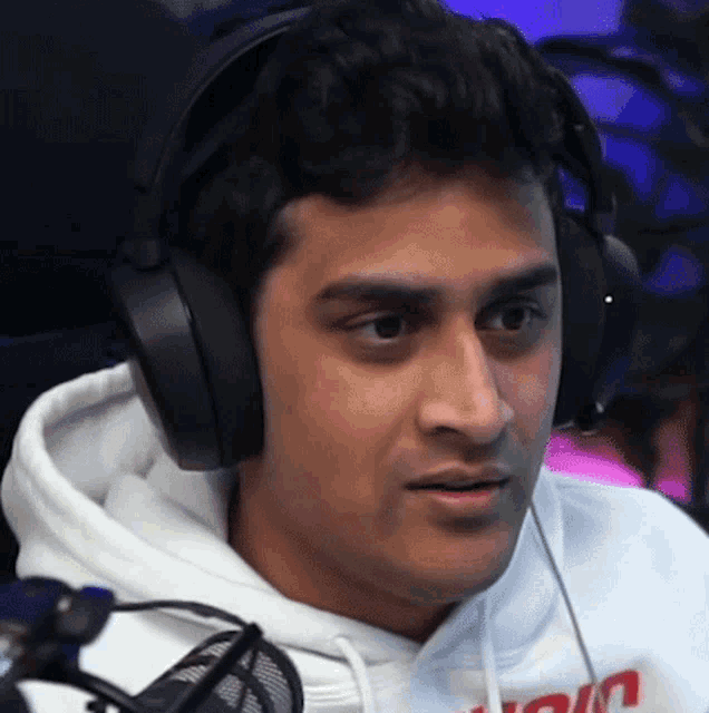 a man wearing headphones and a white hoodie with the word join on it looks at the camera
