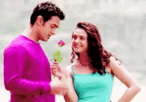 a man in a purple shirt is giving a rose to a woman in a blue tank top .