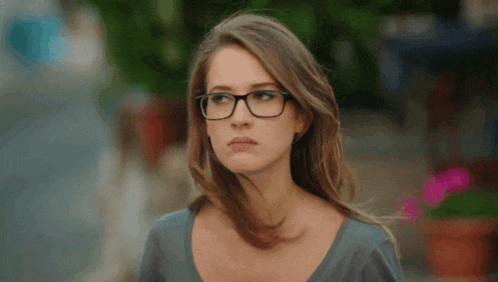 a woman wearing glasses and a blue shirt looks to the side