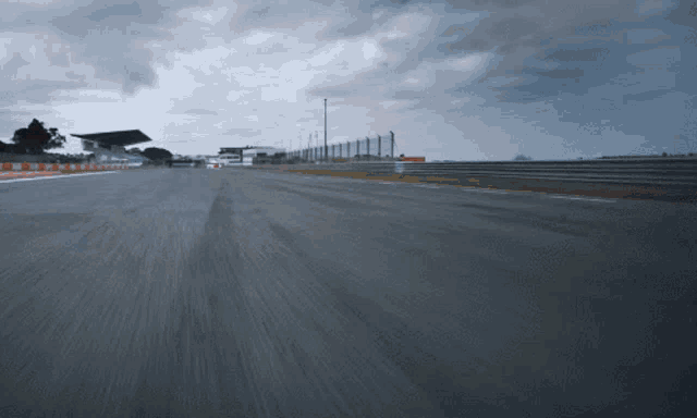 a race track with a cloudy sky and a fence