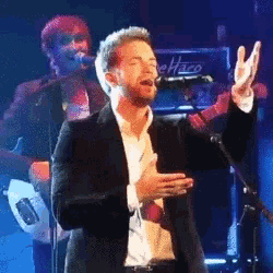 a man in a suit is singing into a microphone with a fender amplifier in the background