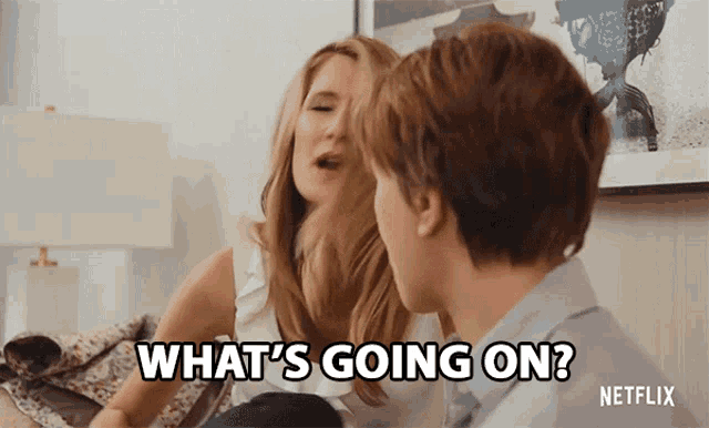 a man and a woman are sitting on a couch and the woman says what 's going on