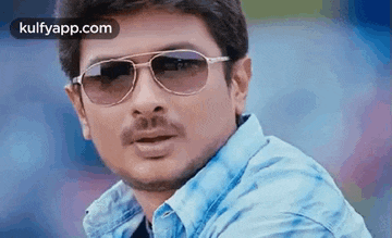 a man wearing sunglasses and a blue shirt looks at the camera .