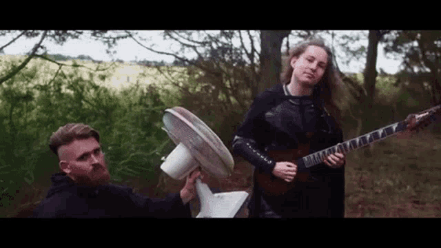 a man is holding a fan in front of a man playing a guitar .